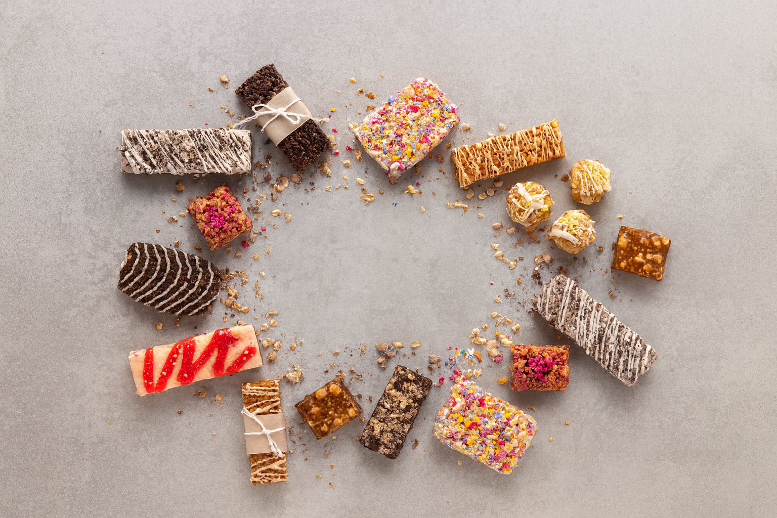 Assorted colorful candies and chocolates arranged in a circle on a gray surface.