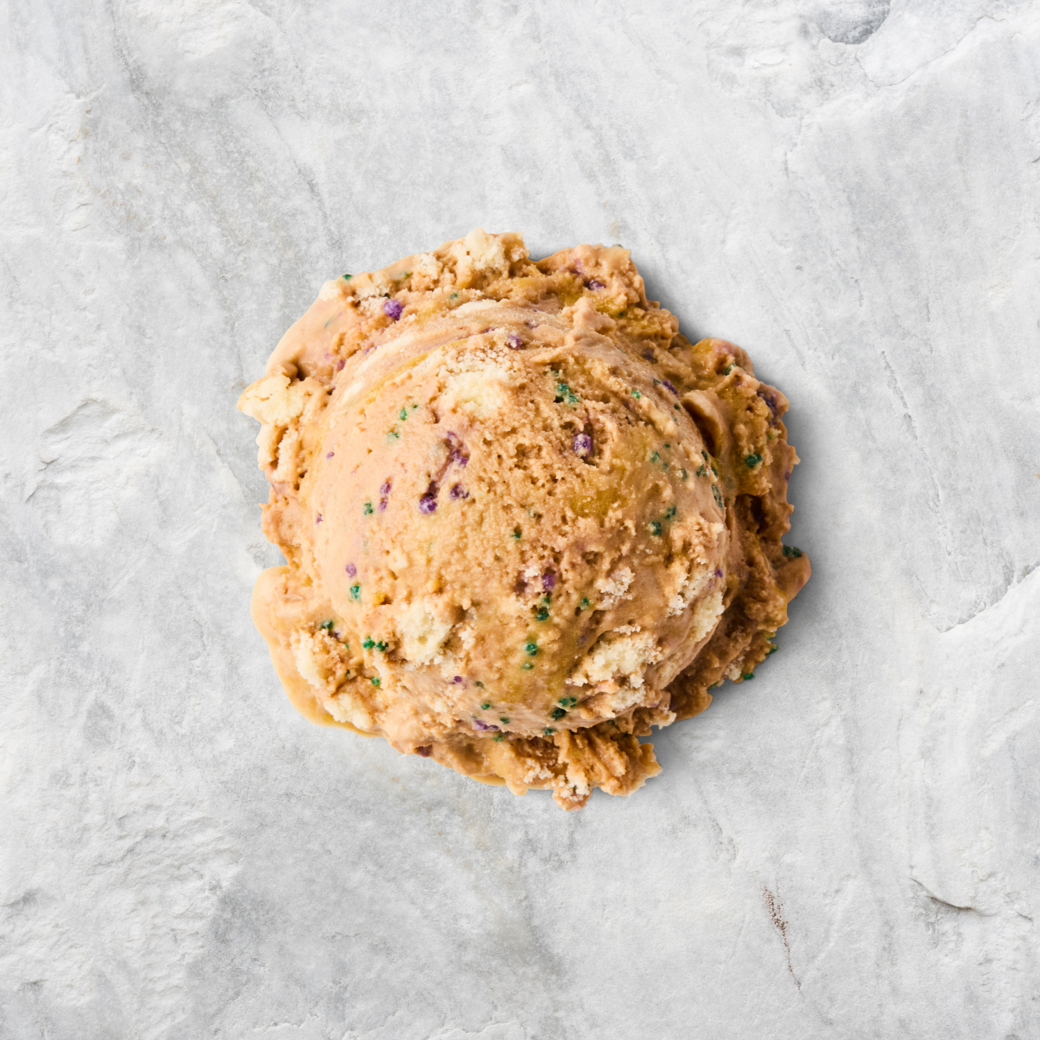 A scoop of birthday cake flavored ice cream with rainbow sprinkles on a light gray textured surface.