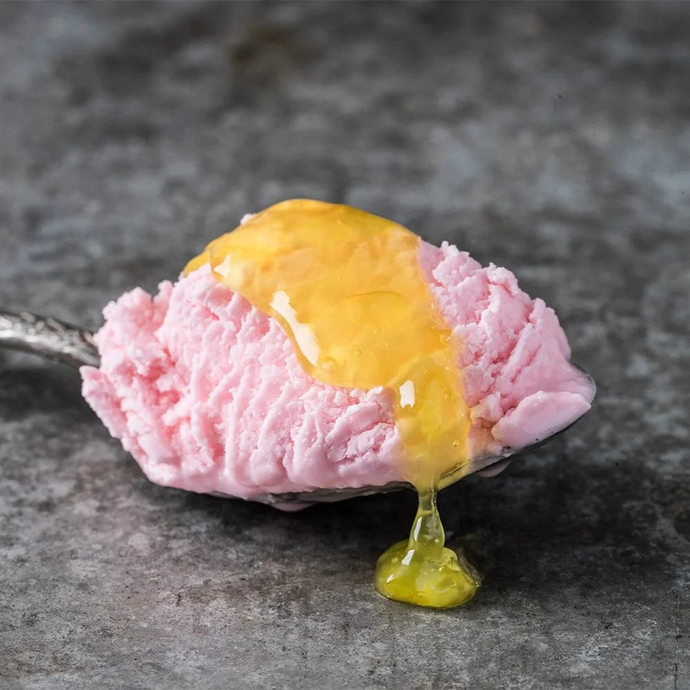 Close-up of a pink scoop of ice cream with honey drizzling down onto a gray surface.
