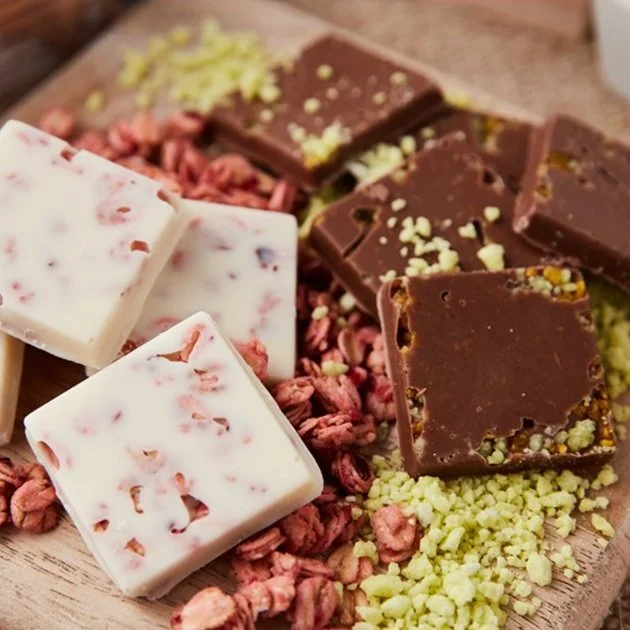 Assorted chocolate bars with nuts and dried berries on a wooden board.