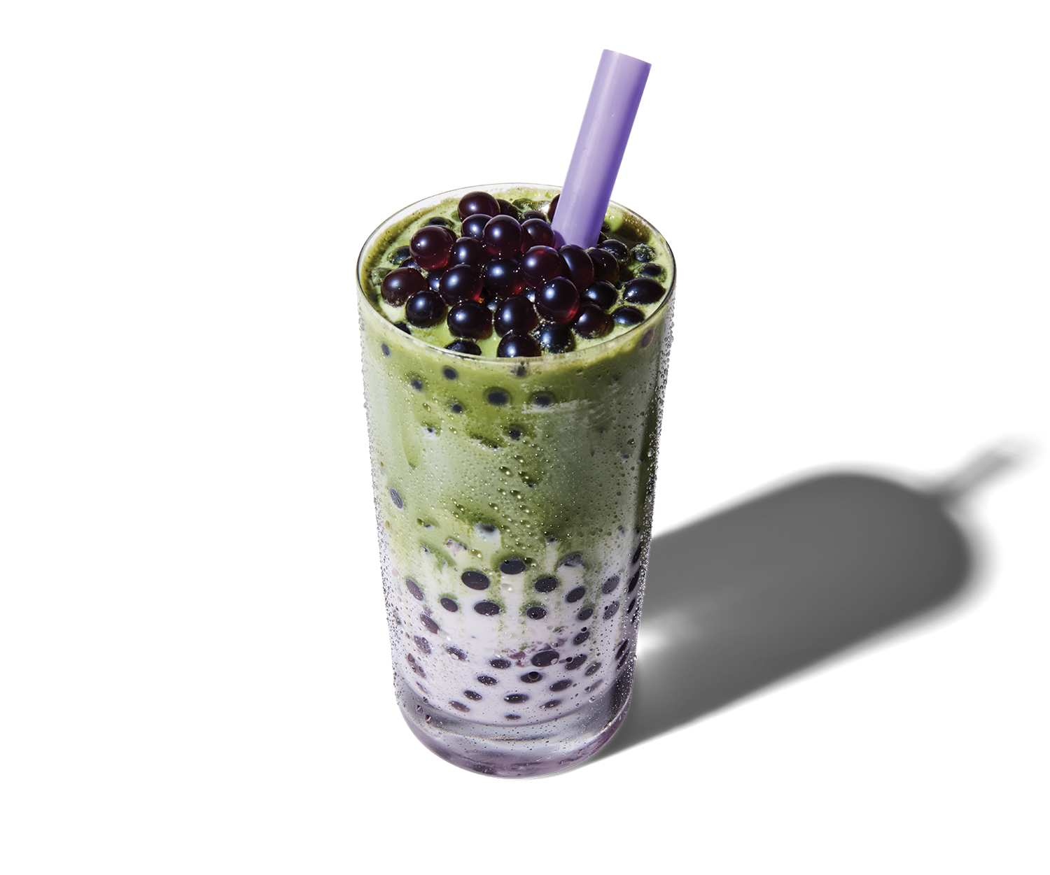A tall glass of bubble tea with black tapioca pearls at the bottom, topped with green tea and black tapioca pearls, with a purple straw.
