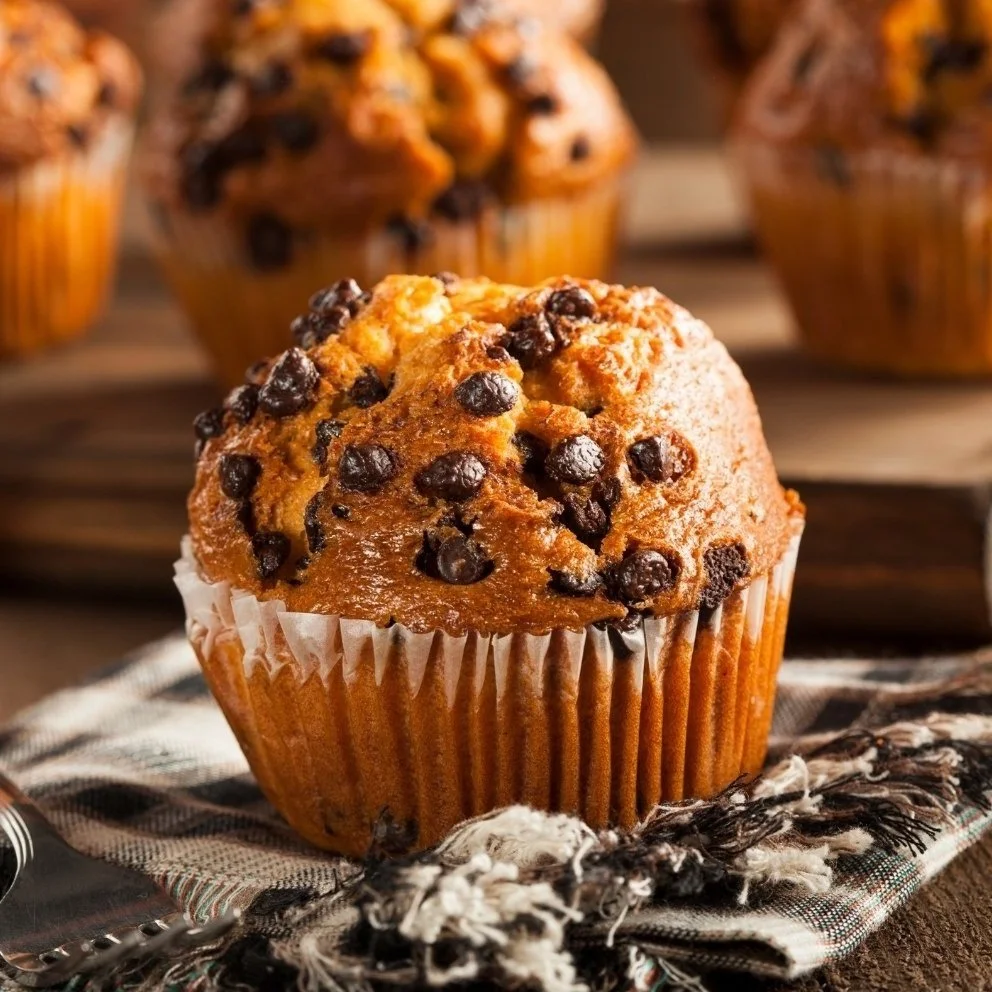 Close-up of a chocolate chip muffin on a cloth napkin, with more muffins in the background.
