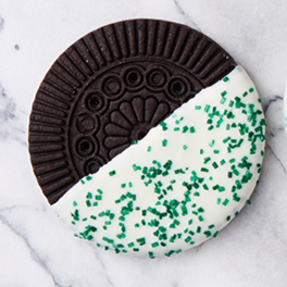 Half of a chocolate sandwich cookie with green sprinkles on white icing.