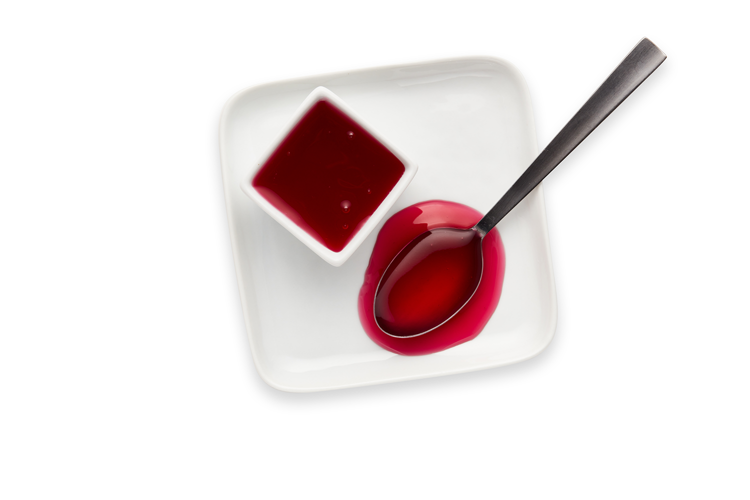 A white square plate with a small square dish of red sauce and a silver spoon, with red sauce spilled on the plate.