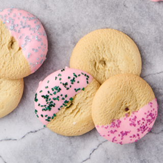 Cookies with pink and yellow icing, decorated with sprinkles, on a gray surface.