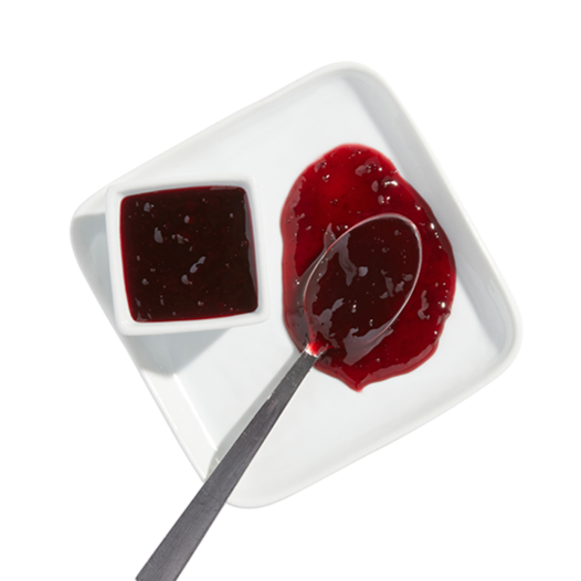 A white square dish containing two sections: one with dark red berry jam and the other with red jelly, with a spoon resting on the jelly.