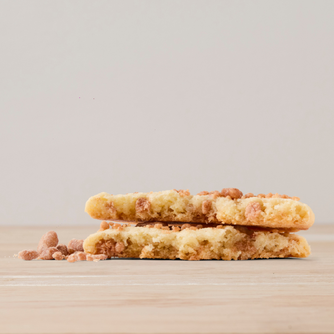 Two cookies stacked on top of each other on a light wood surface with bits of cookie crumbs around