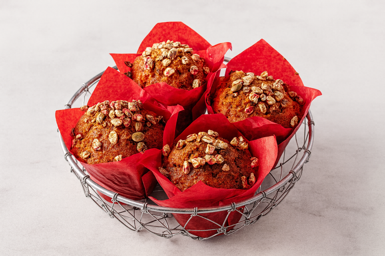 Four muffins topped with oats in a metal basket lined with red paper