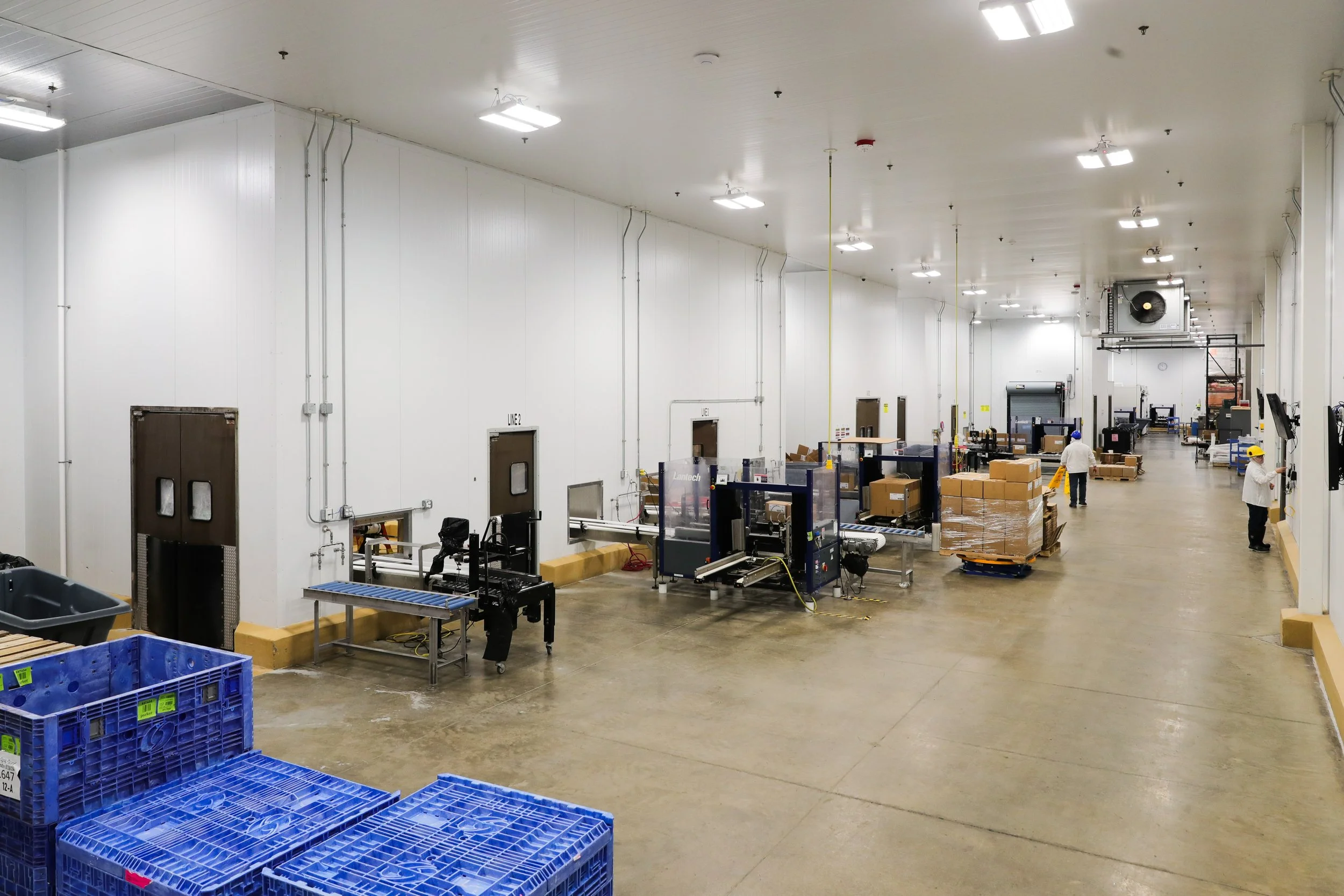 Large warehouse with unloading area, workers, conveyor belts, and stacked boxes.