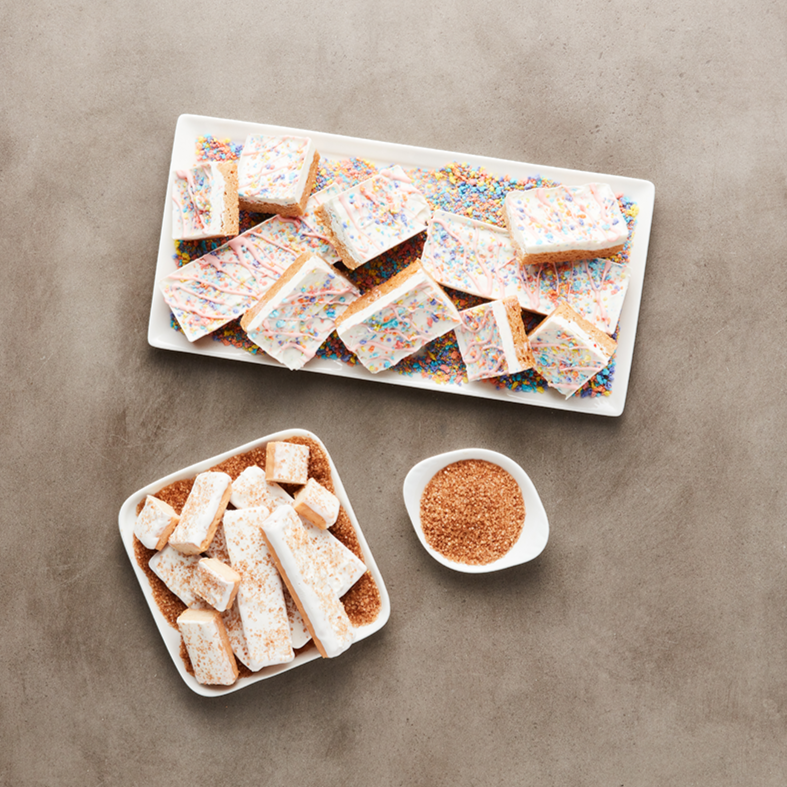 Assorted colorful rice Krispies treats and crushed graham cracker crumbs on a neutral background.