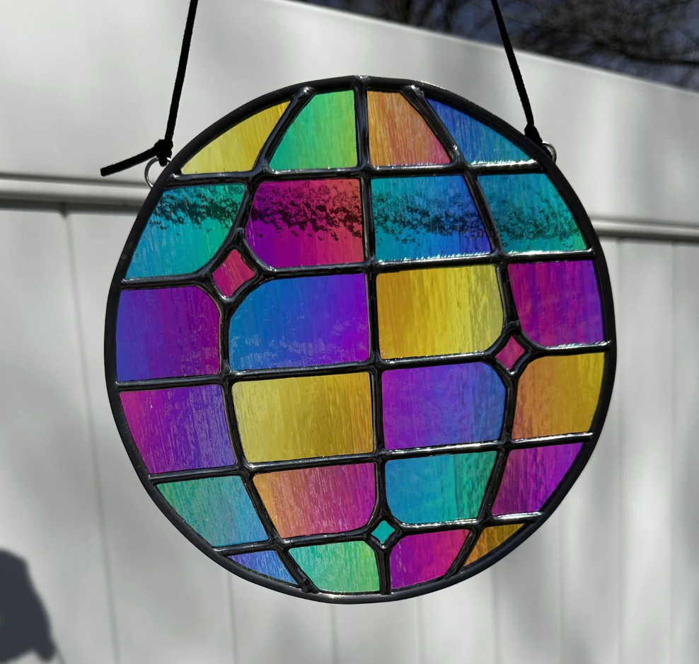 Colorful stained glass art piece resembling a disco ball hanging outdoors with a white background.