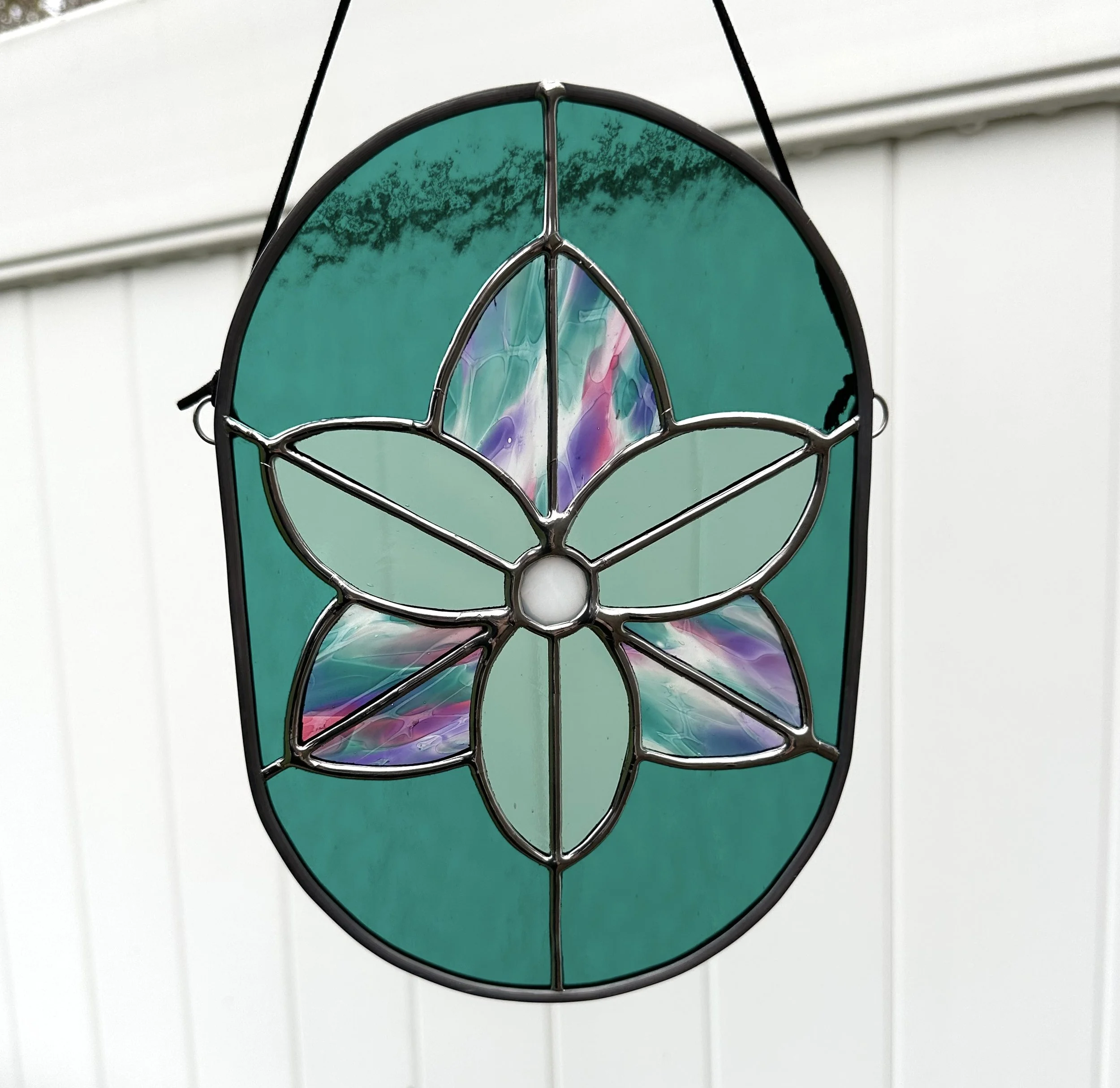 Colorful stained glass hanging ornament with a floral design, featuring a flower with four large petals and a central circle, set against a light background.