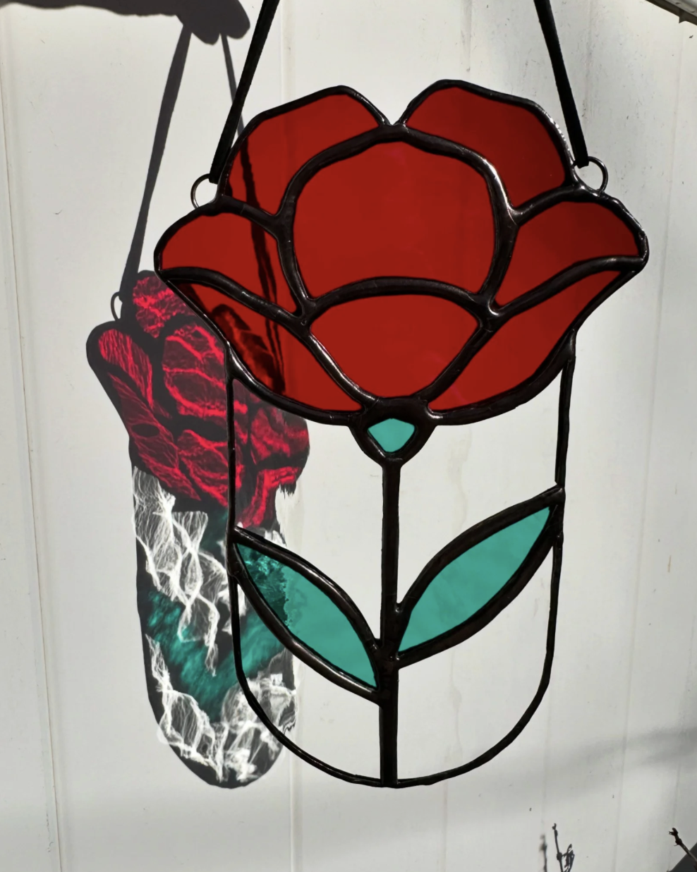 Colorful stained glass floral lamp with red petals and green leaves, casting a shadow on a white wall.