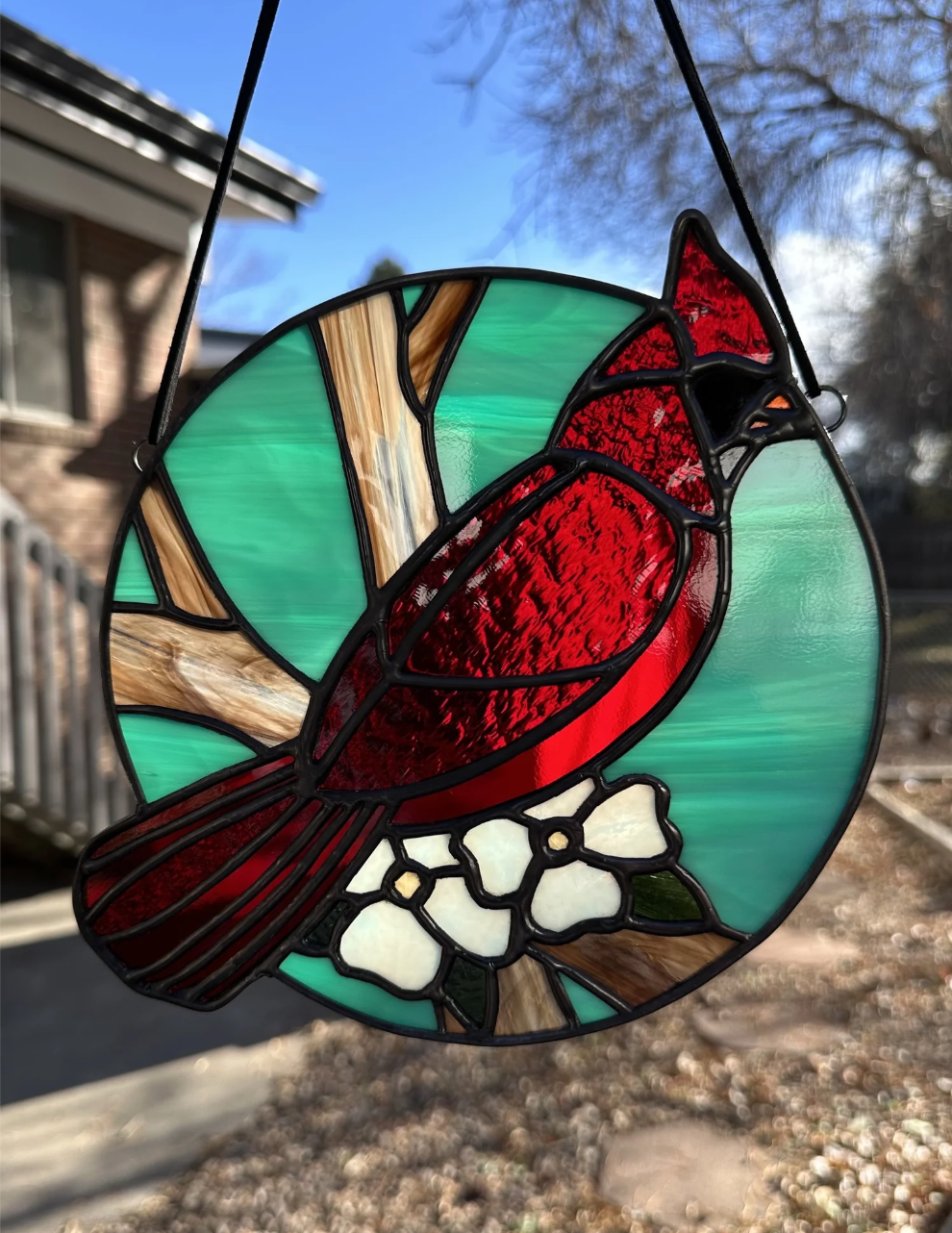 Stained glass hanging decoration of a red cardinal bird with white flowers and a green background.