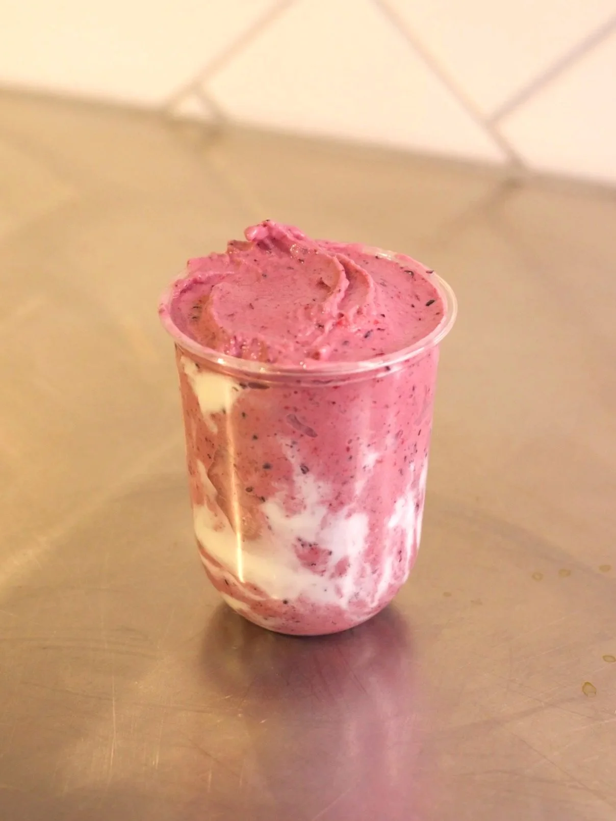 Layered dessert in a glass with pink and white swirls and a creamy topping.