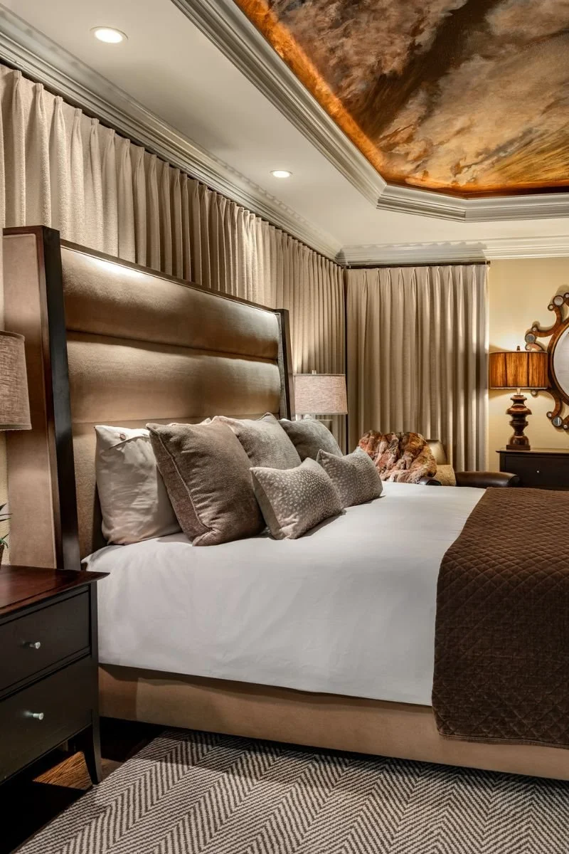 Another view of the primary bedroom with upholstered headboard dressed in chocolates and creams