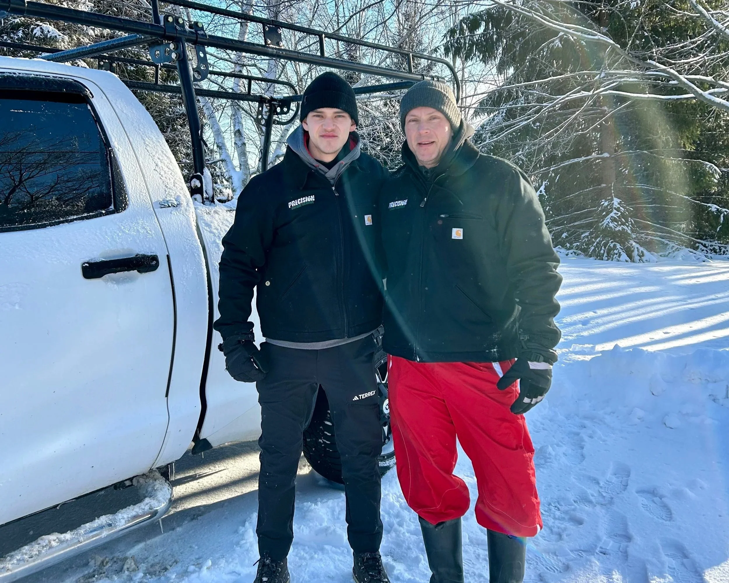 Two men standing outside in snowy landscape, near a snow-covered vehicle, dressed in winter clothing, posing for a photo.