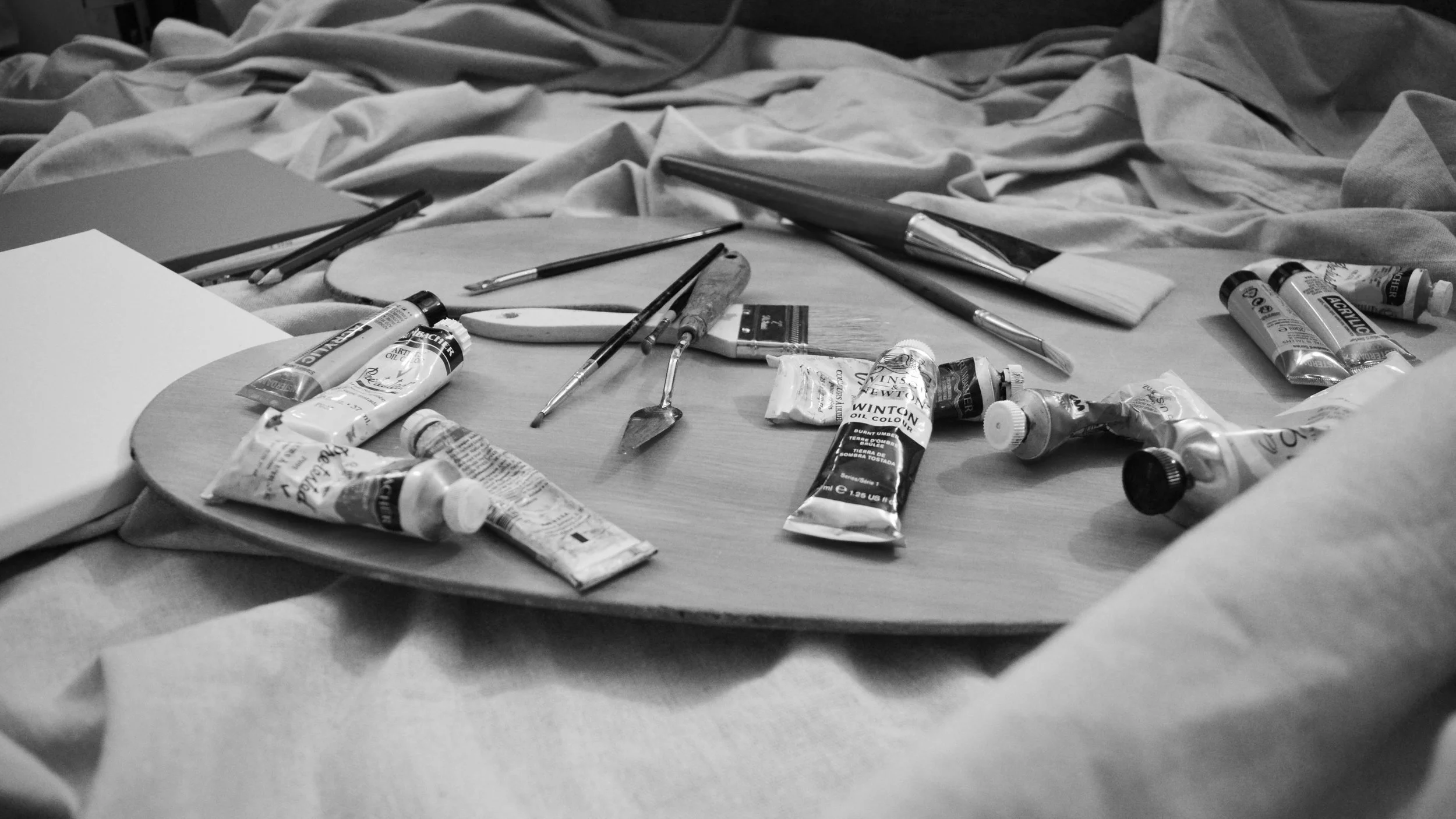 Art supplies including tubes of oil paint, paintbrushes, and a palette on a table.