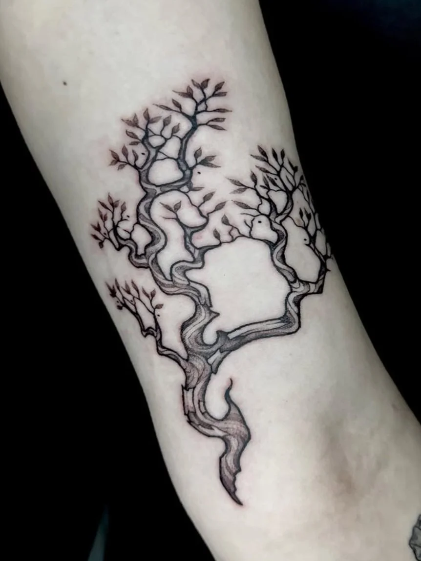 Black and gray tattoo of a stylized tree with twisted branches and leaves on light skin.