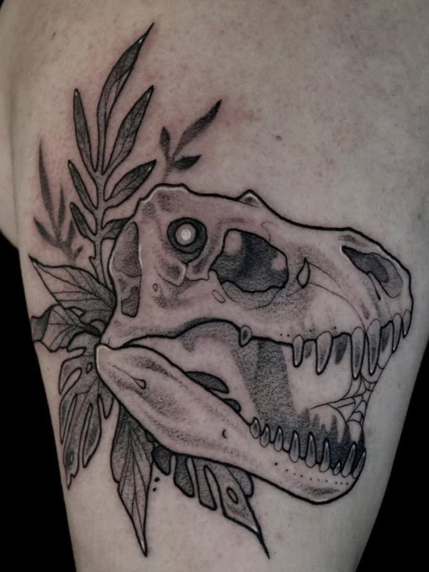 Tattoo of a dinosaur skull with leaves surrounding it.