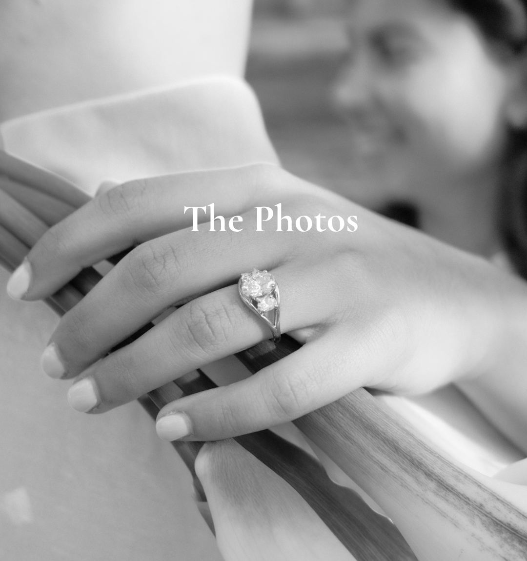 Close-up of a woman's hand with an engagement ring, holding wooden railing, blurred woman smiling in background, black and white photo.