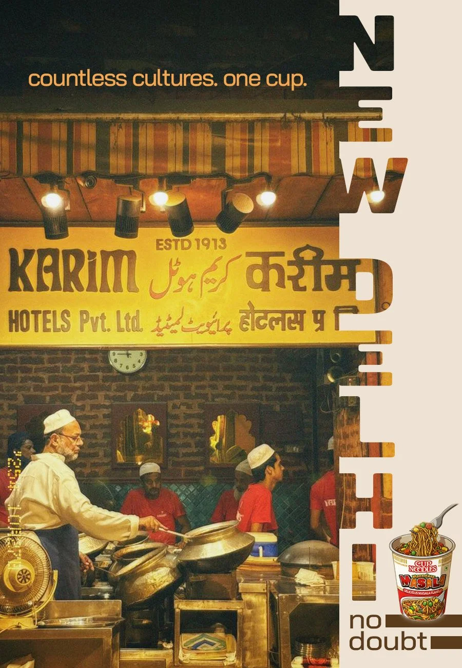 A restaurant kitchen scene with a man cooking and several workers in red uniforms. A yellow sign above features multilingual text, including 'Karim Hotels Pvt. Ltd.' and the establishment's founding year, 1913. The interior has brick walls, mirrors, and hanging lights.
