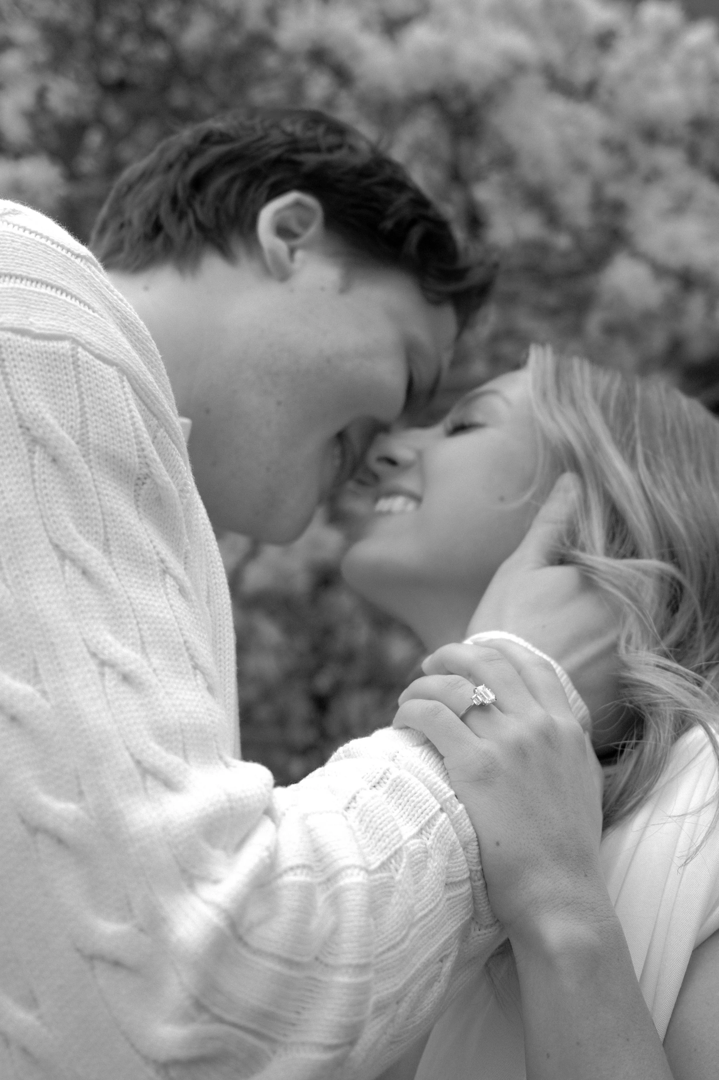 A black-and-white photo of a man and a woman sharing a joyful moment, their foreheads touching, both smiling and holding each other's hands.