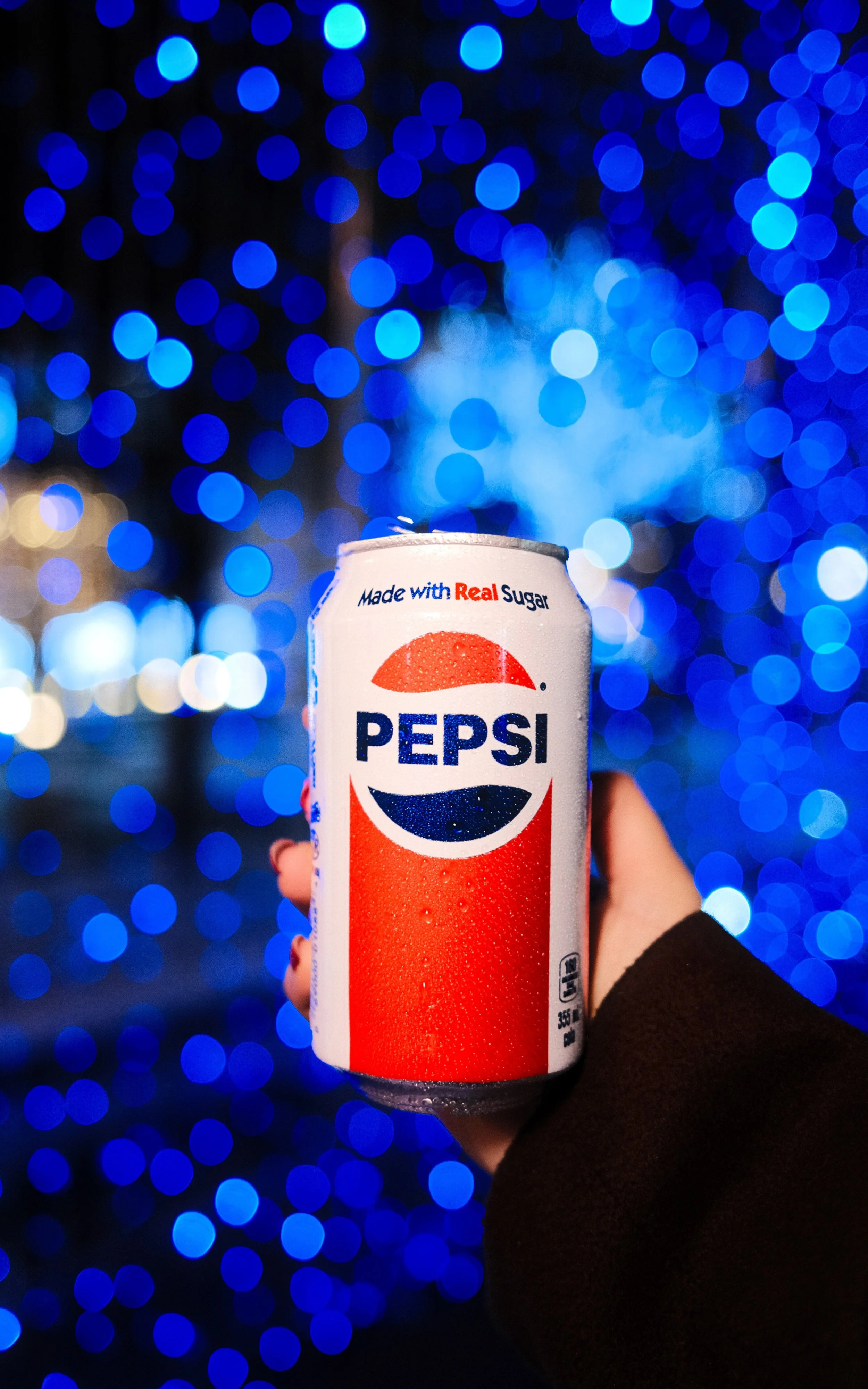 A hand holding a can of Pepsi with a blue bokeh background.