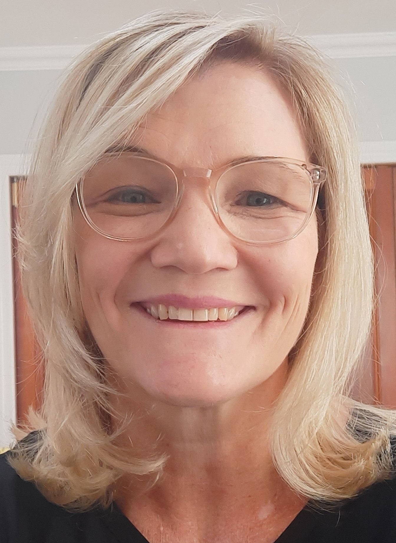 Smiling woman with glasses and blonde hair indoors.