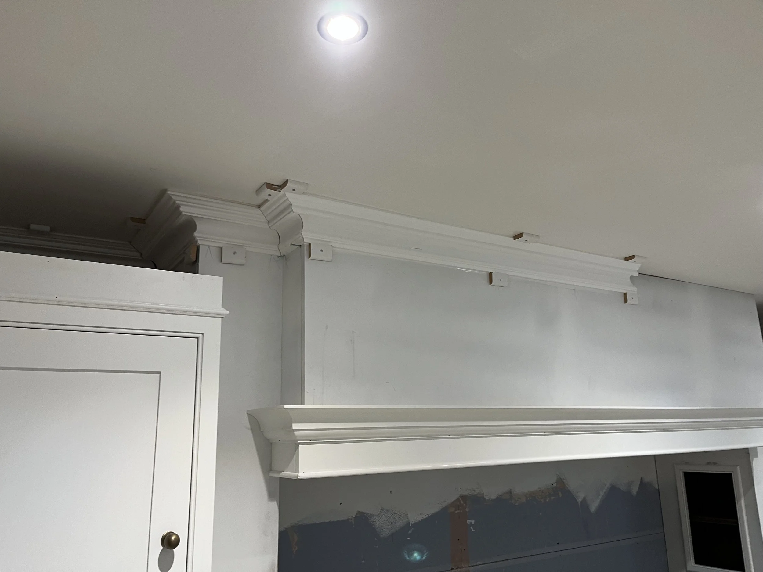 Room under construction with white crown molding and trim, partially painted wall, and a ceiling light.