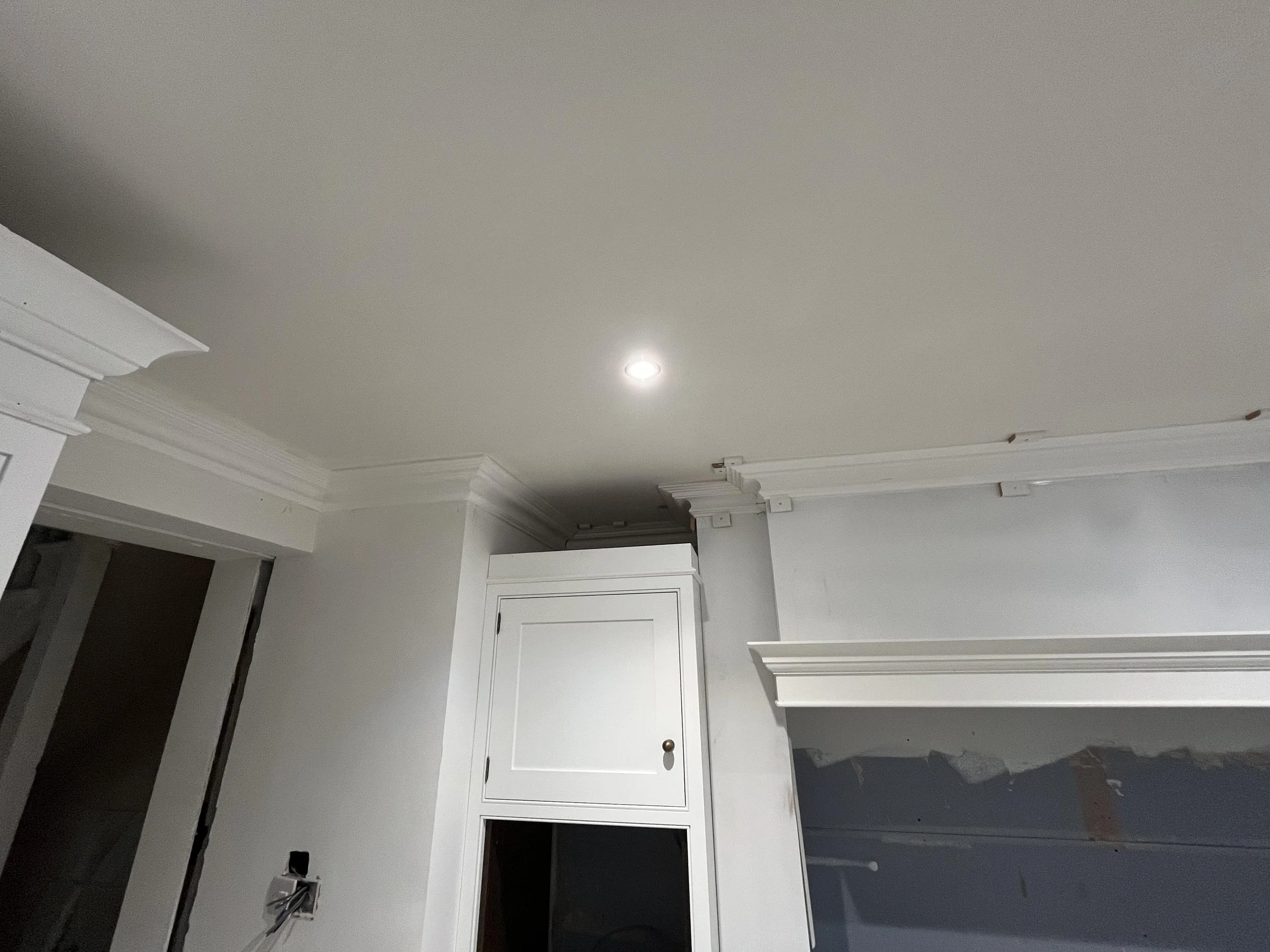 Ceiling with crown molding and a recessed light in a room with white walls and cabinetry.