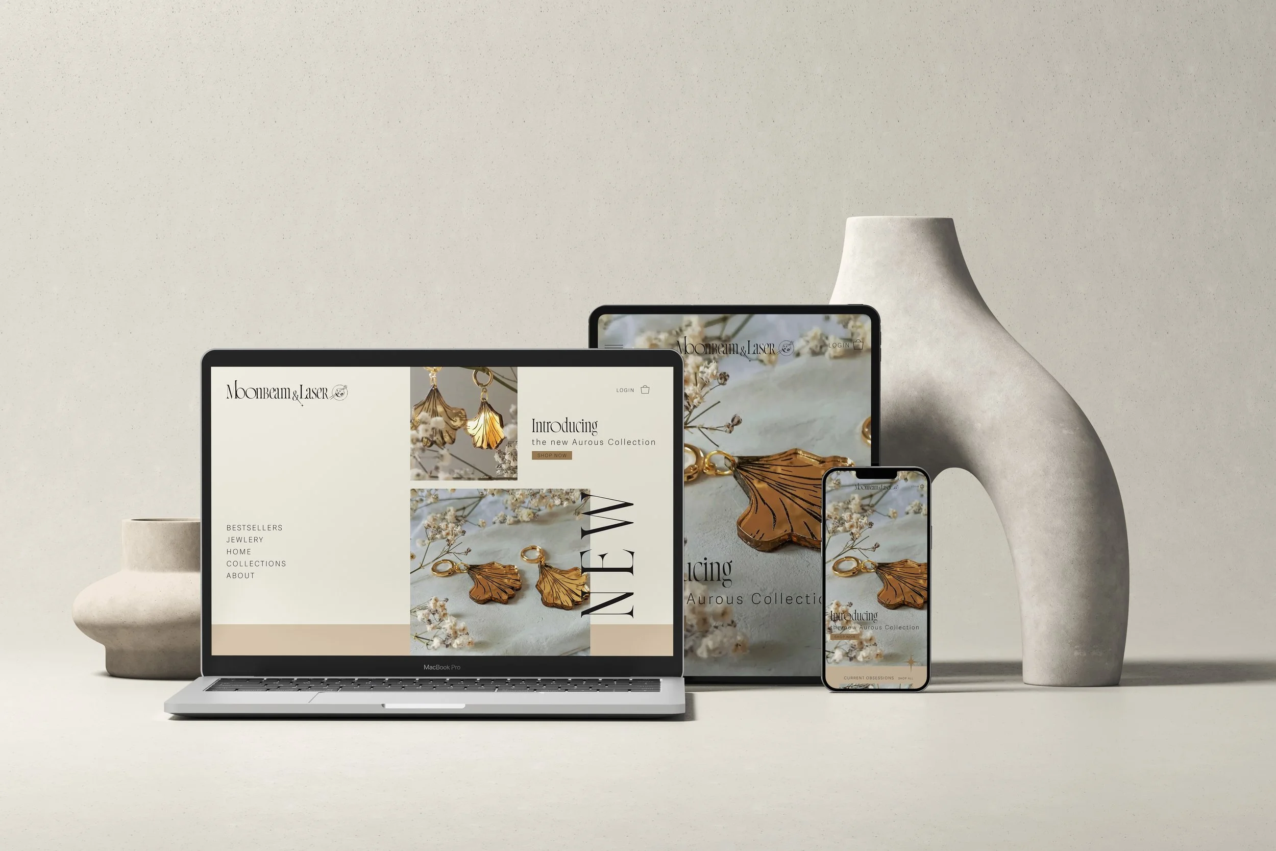 A digital display with a jewelry website open, showing earrings and jewelry items on a light background, with a laptop, tablet, and phone on a neutral surface against a minimalistic backdrop.