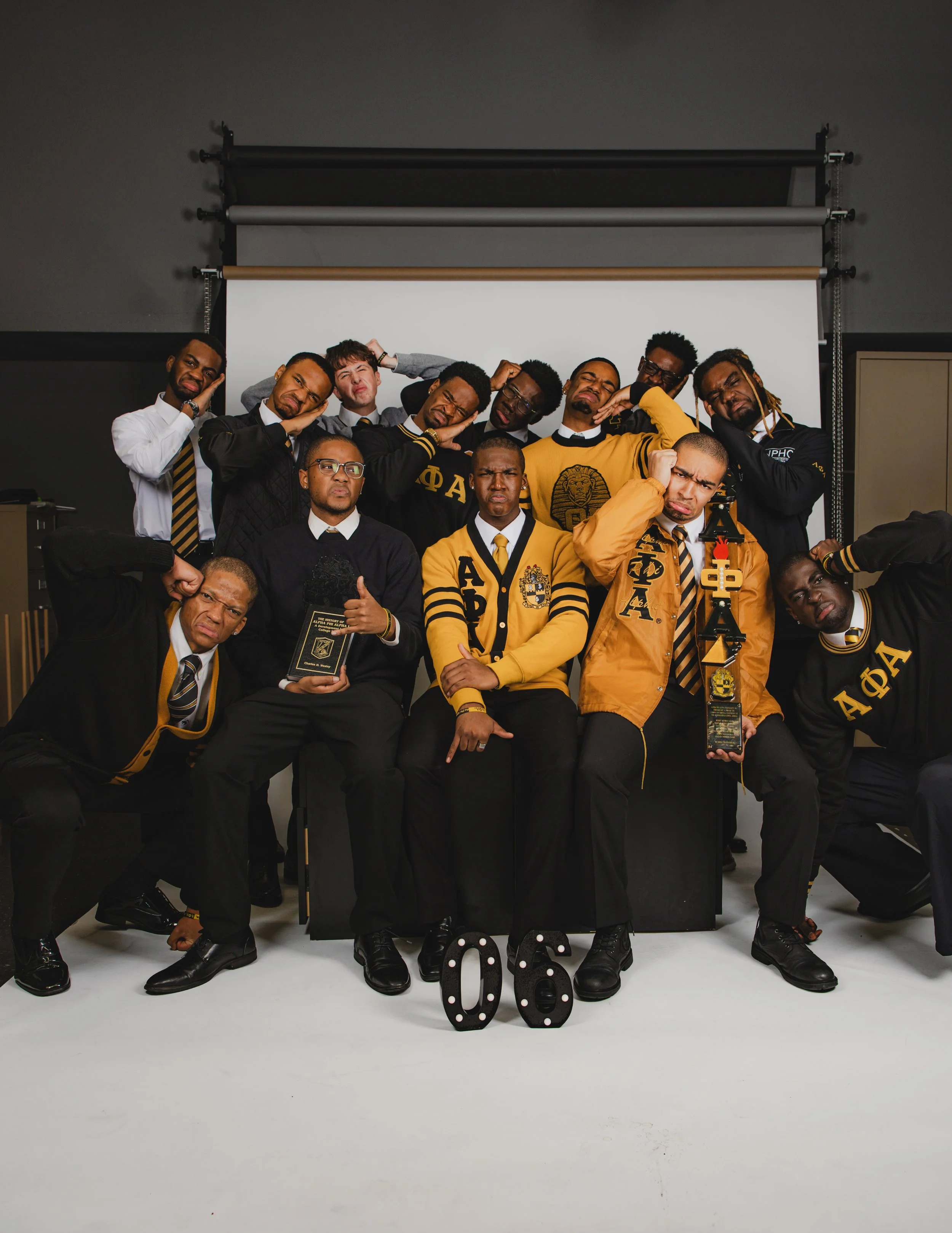 Group of diverse young adults posing together in a photoshoot studio, making funny faces and gestures, with the number '06' displayed on the floor.