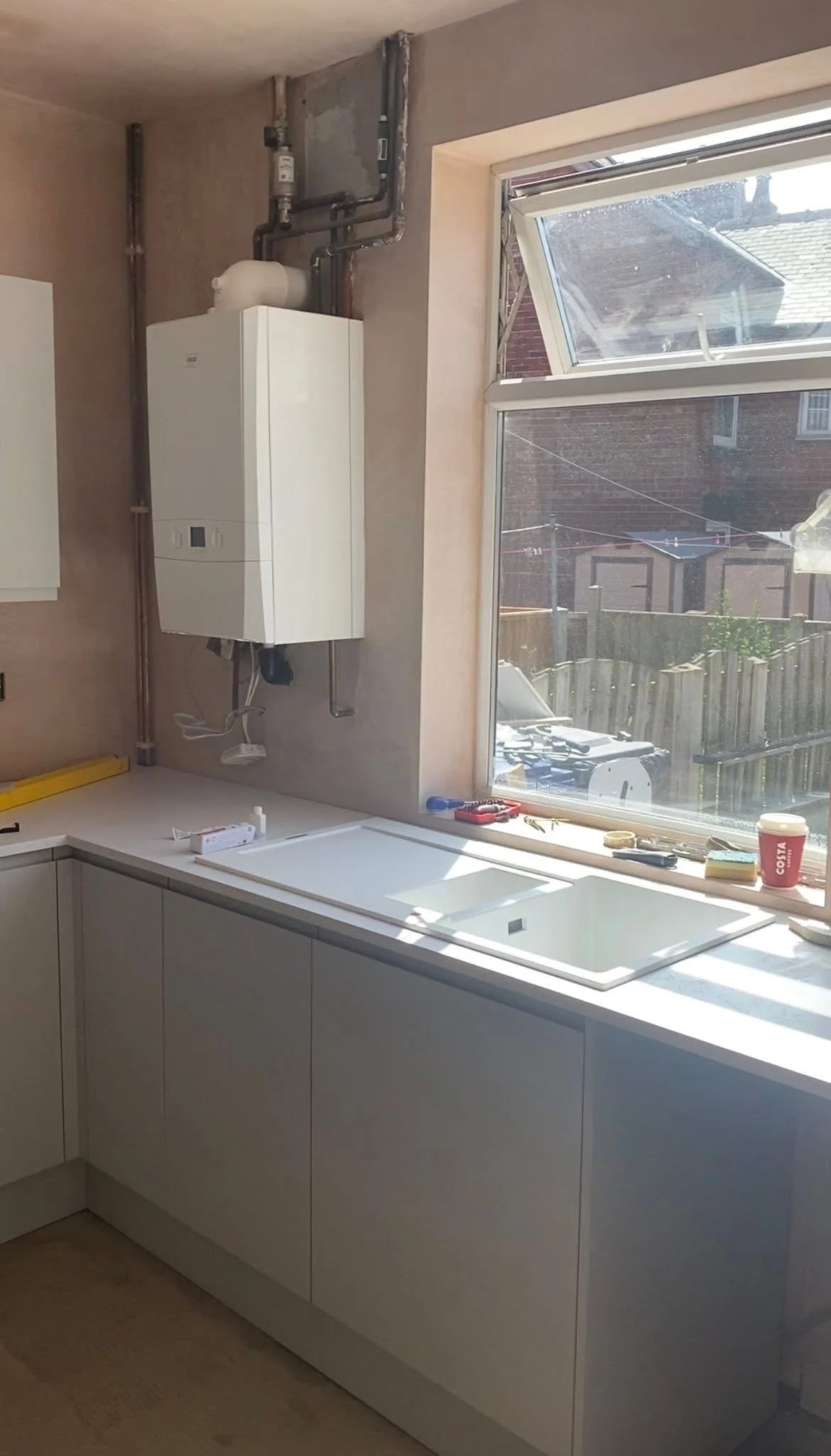 A kitchen with unfinished cabinetry, an open window, and a mounted boiler system on the wall.