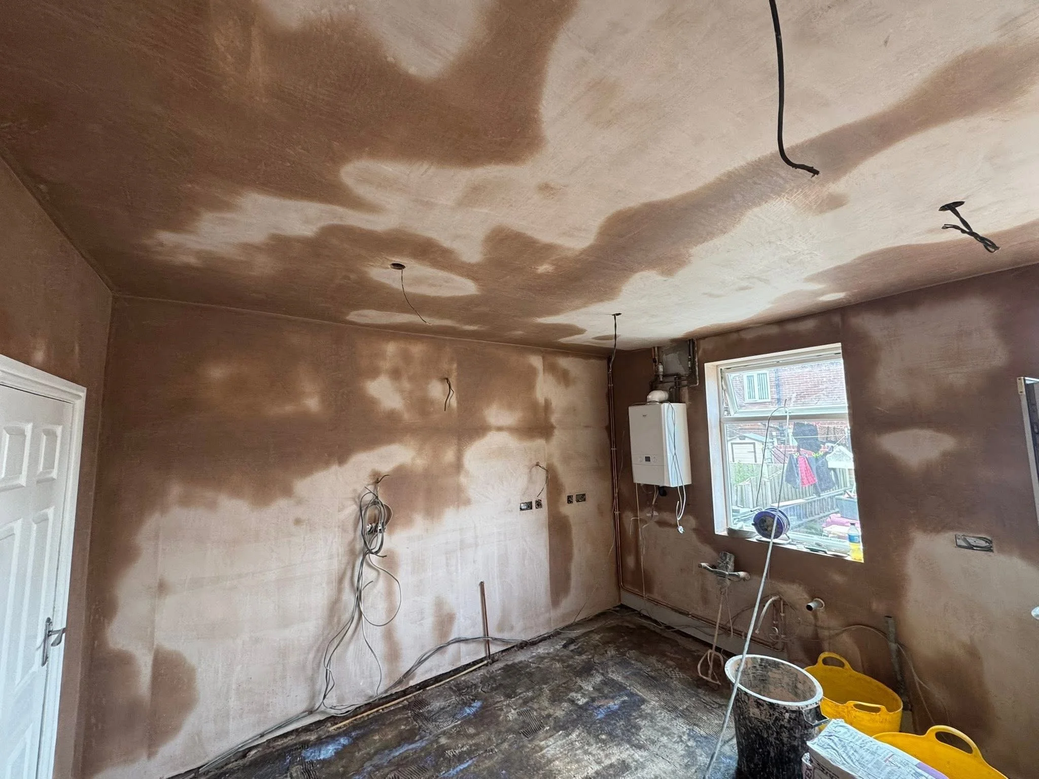 Room under renovation with exposed wires, unpainted walls, and construction supplies.