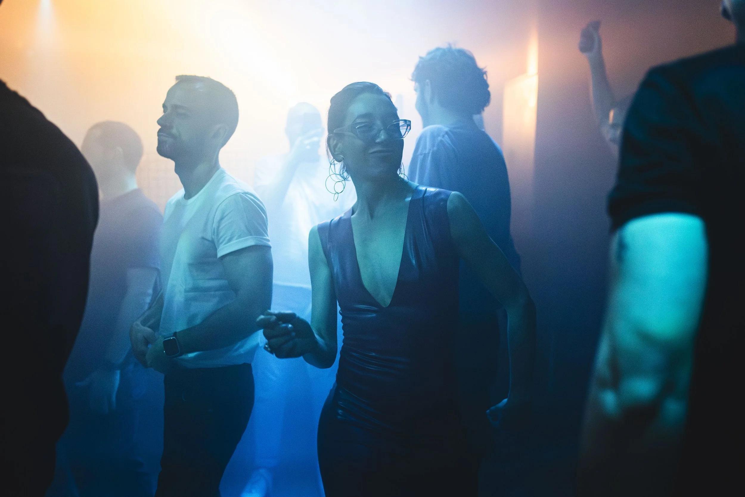 People dancing and enjoying themselves at a party or nightclub with colorful lighting.