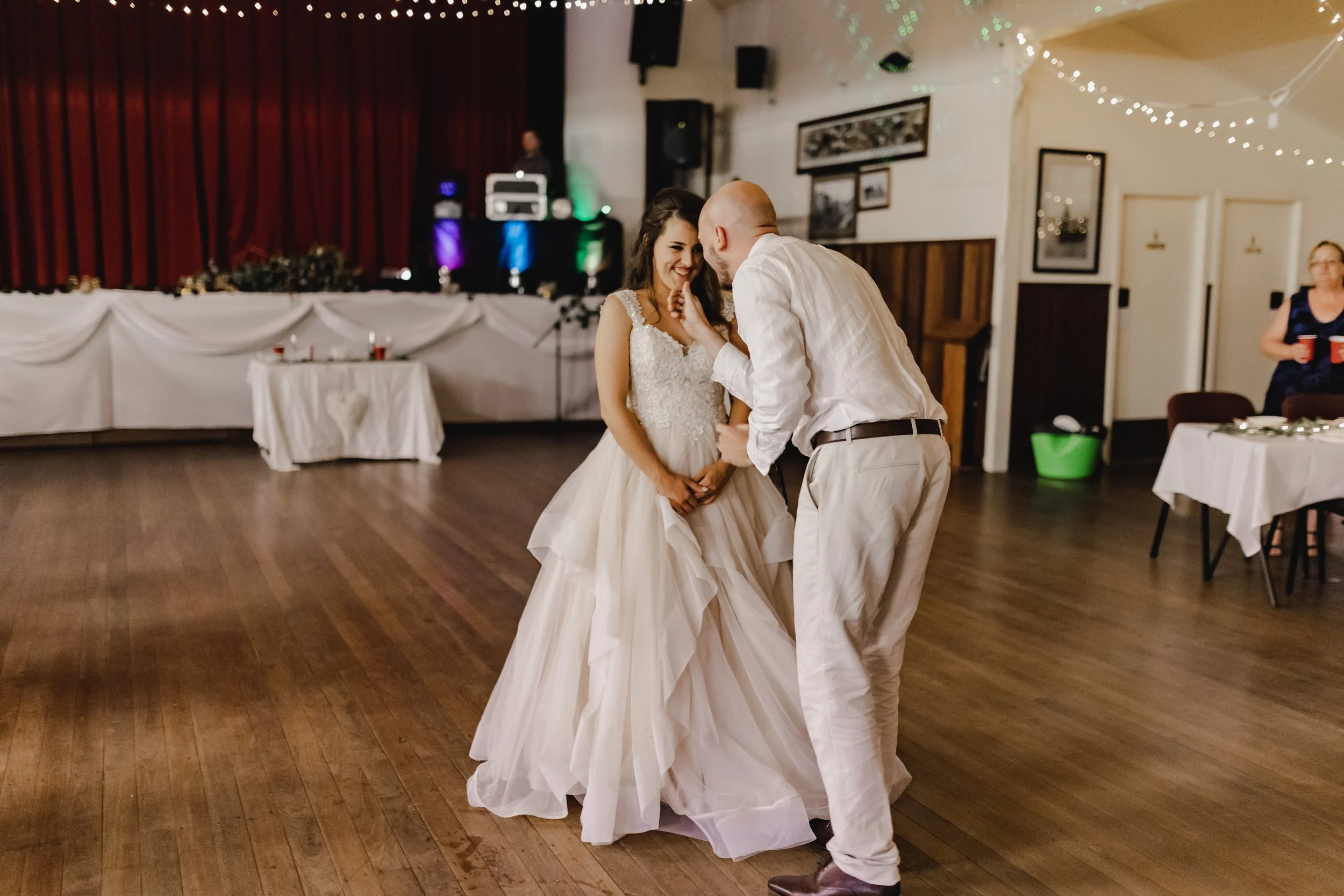 A bride and groom share a special moment on the dance floor at a wedding reception, with the bride smiling and holding her hand to her face, while the groom holds her hand.