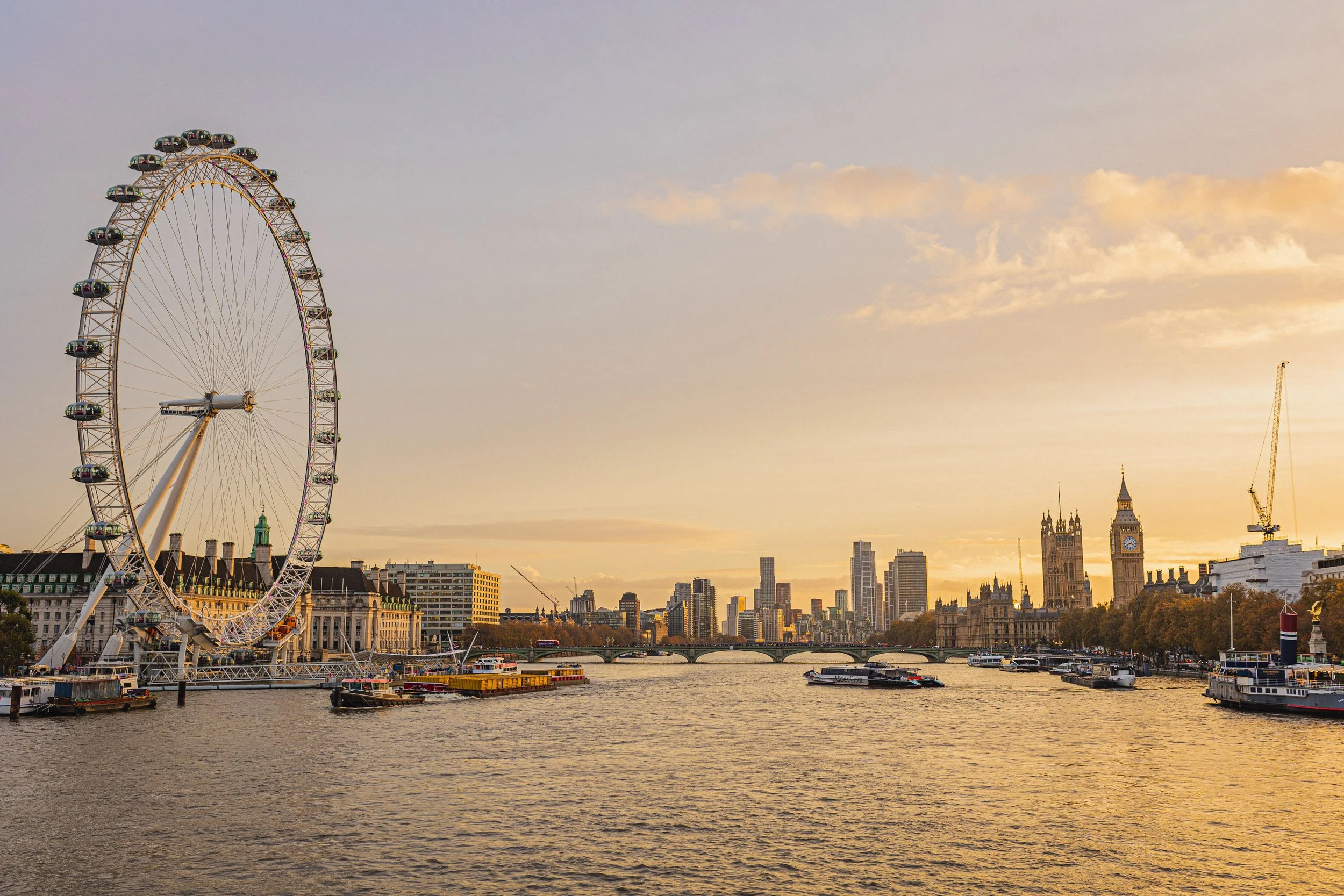 View of the London skyline at sunset with the London Eye Ferris wheel, the River Thames, and the clock tower known as Big Ben.