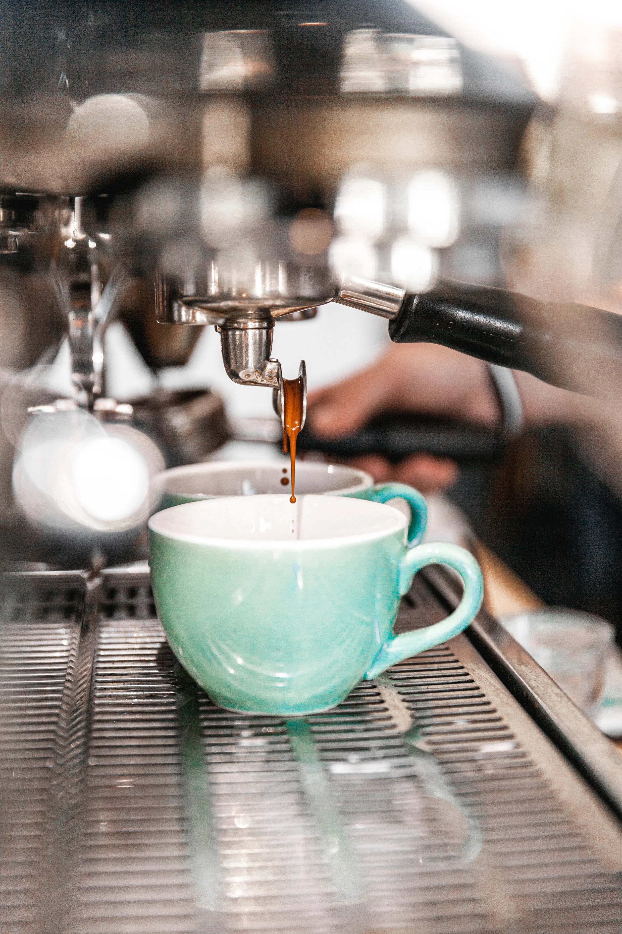 Close-up of coffee being brewed with espresso machine, pouring dark espresso into a green ceramic mug on a metal drip tray.
