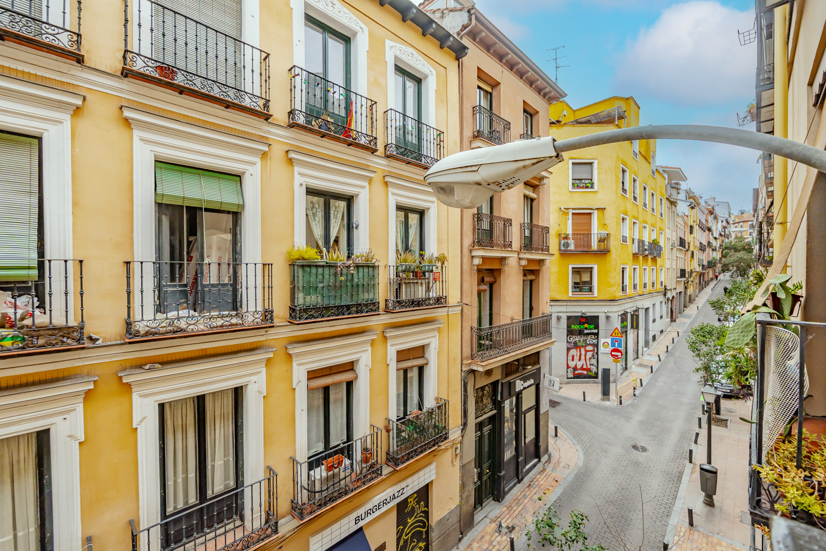 View of a narrow European street with colorful buildings, balconies, and street lamps.