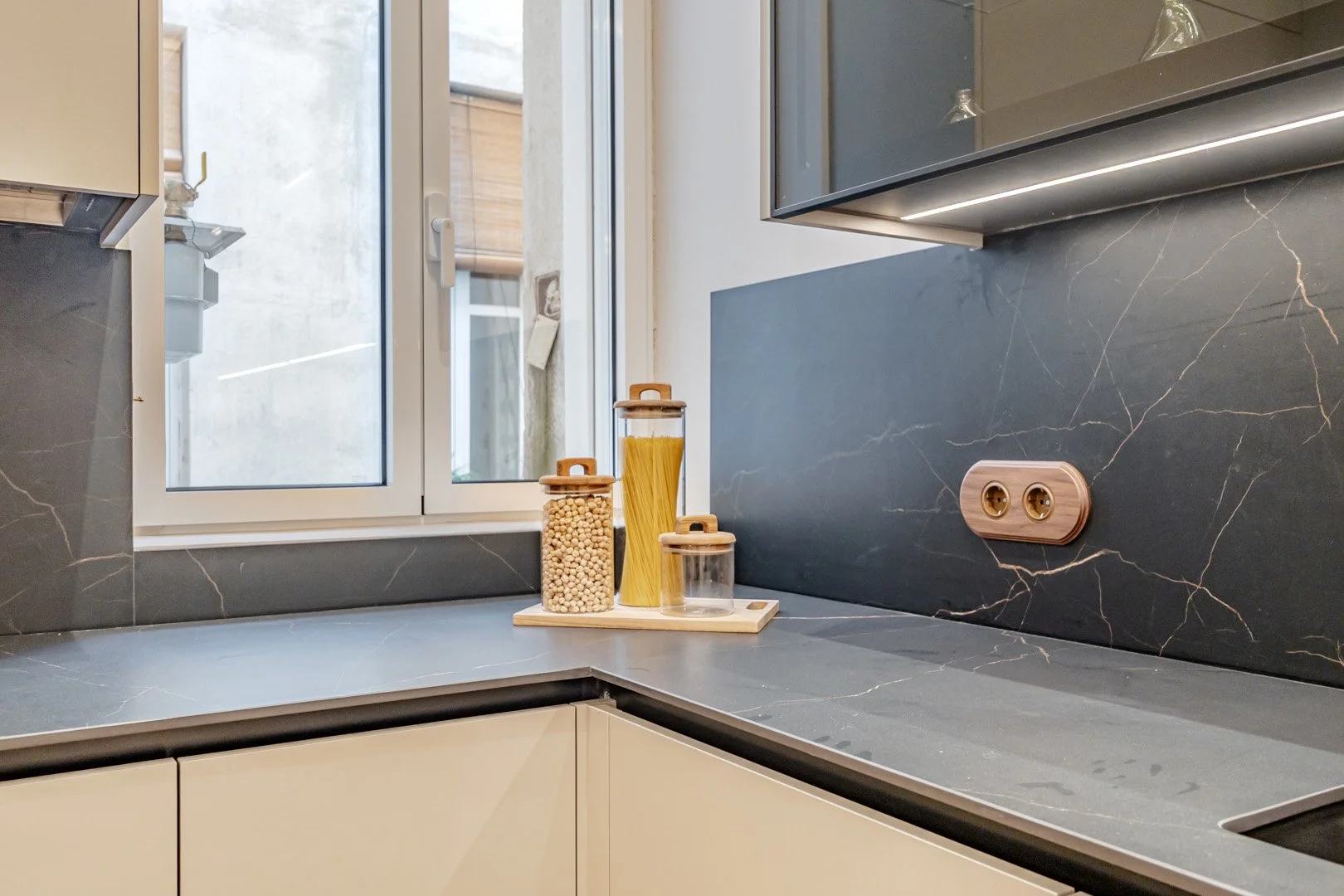 Kitchen countertop with jars of pasta and chickpeas near a window with a view outside. Modern countertops and cabinetry.