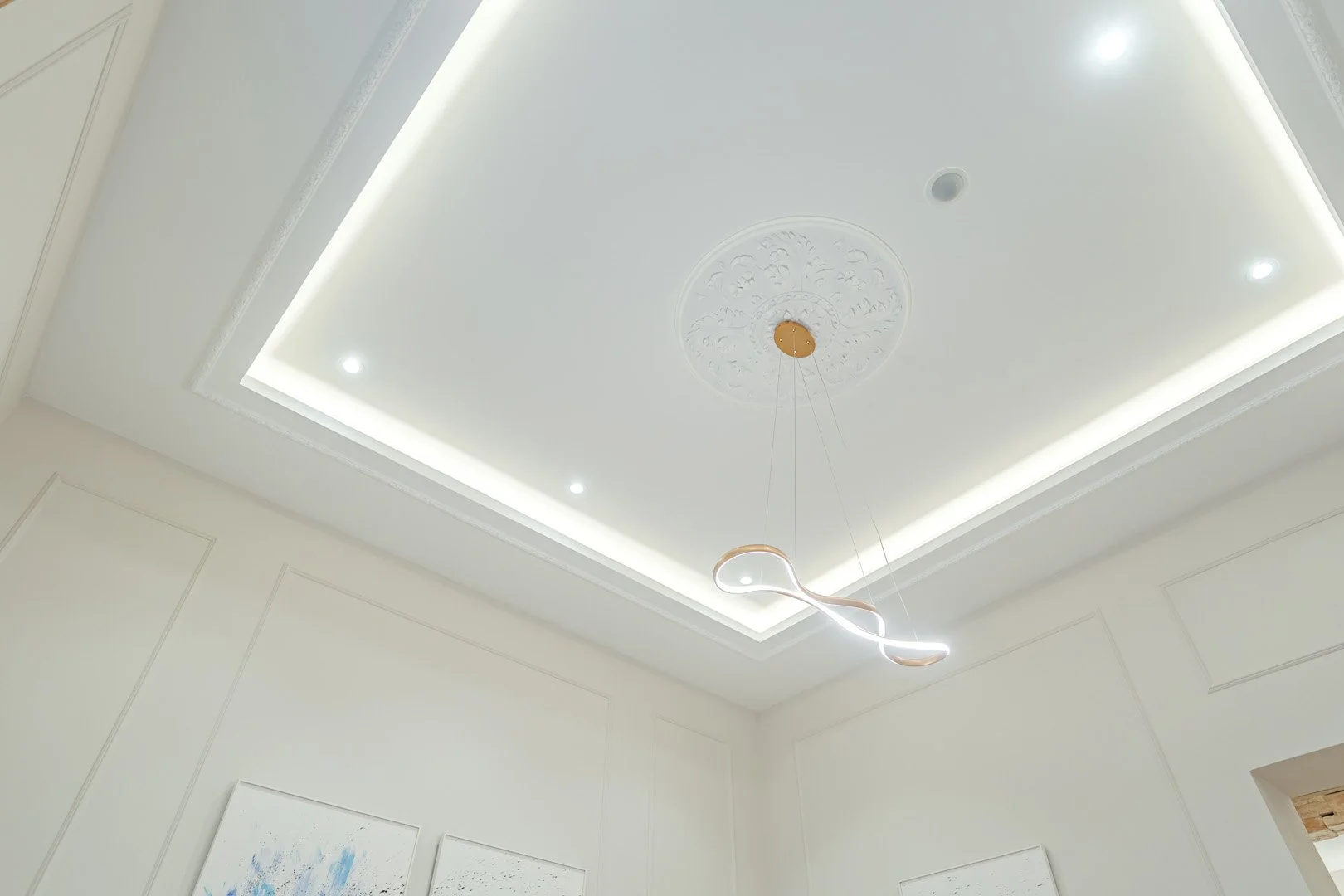 Modern ceiling with recessed lighting, decorative medallion, and a contemporary LED chandelier in a minimalist room.