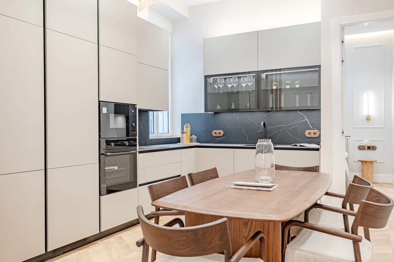 Modern kitchen with beige cabinets, black marble backsplash, and a wooden dining table with chairs.