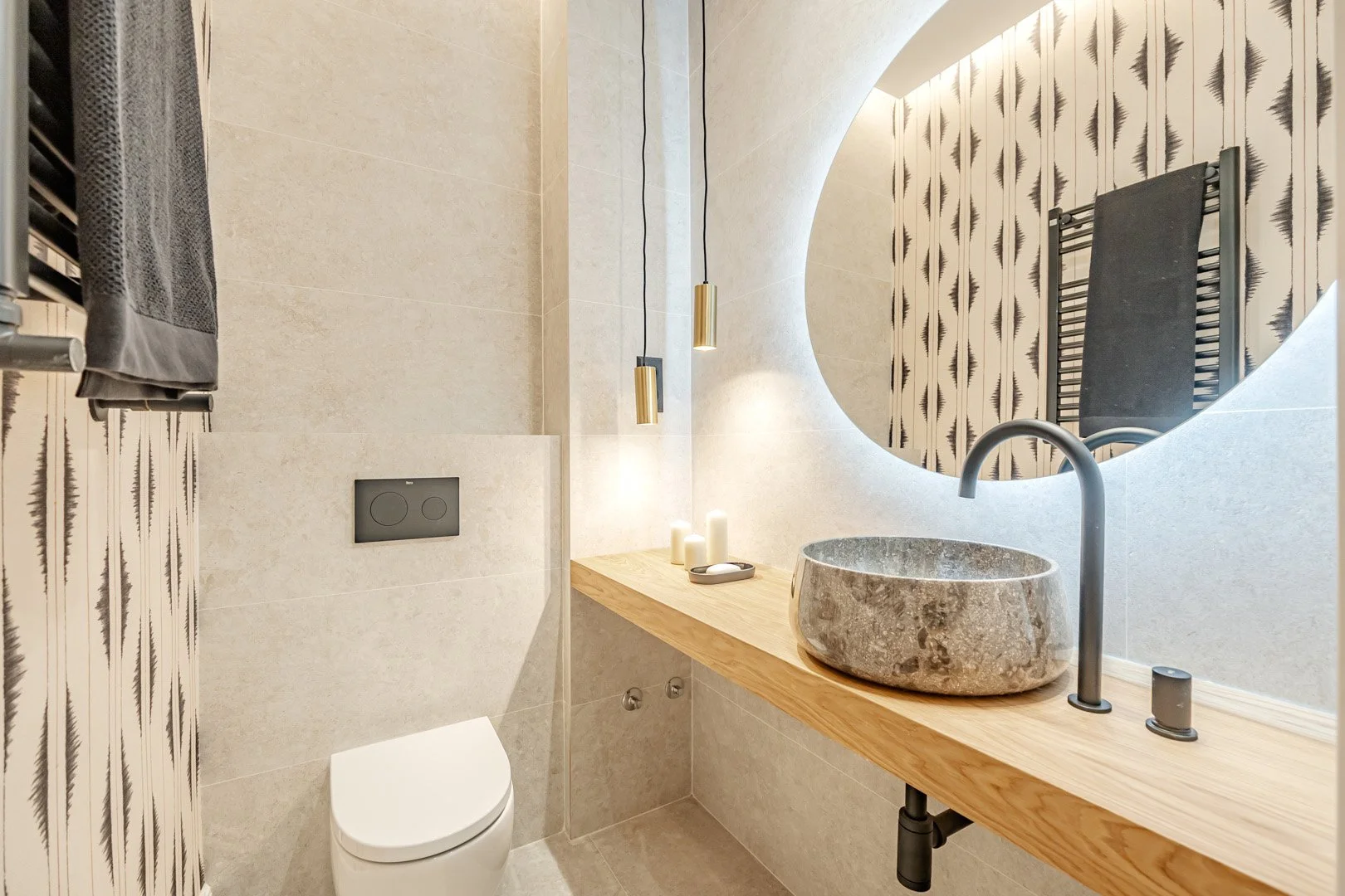 Modern bathroom with a round mirror, stone sink, wooden countertop, and patterned wall behind the mirror.