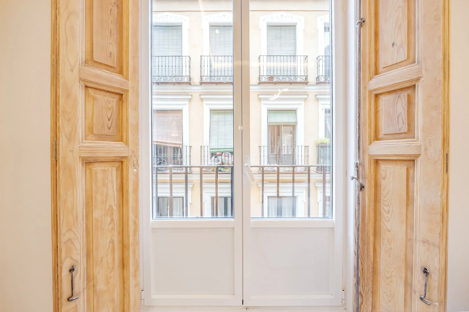 view through a closed glass door with wooden frame, looking out at a neighboring building with balconies and windows