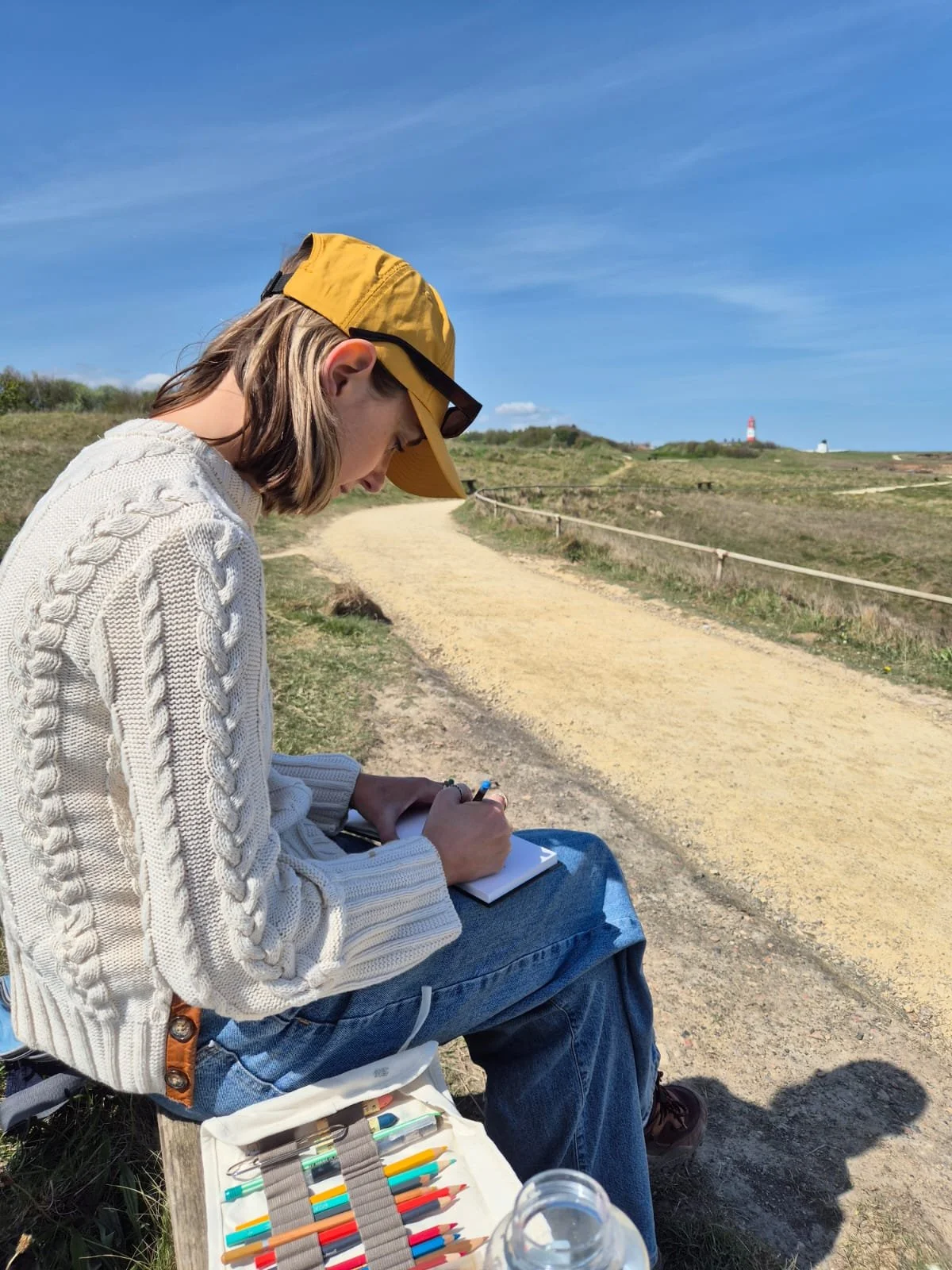 Female illustrator sketching the Northern England coastline outdoors on a summer day