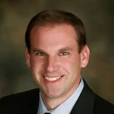 Portrait of a smiling man in a suit with a blurred background.