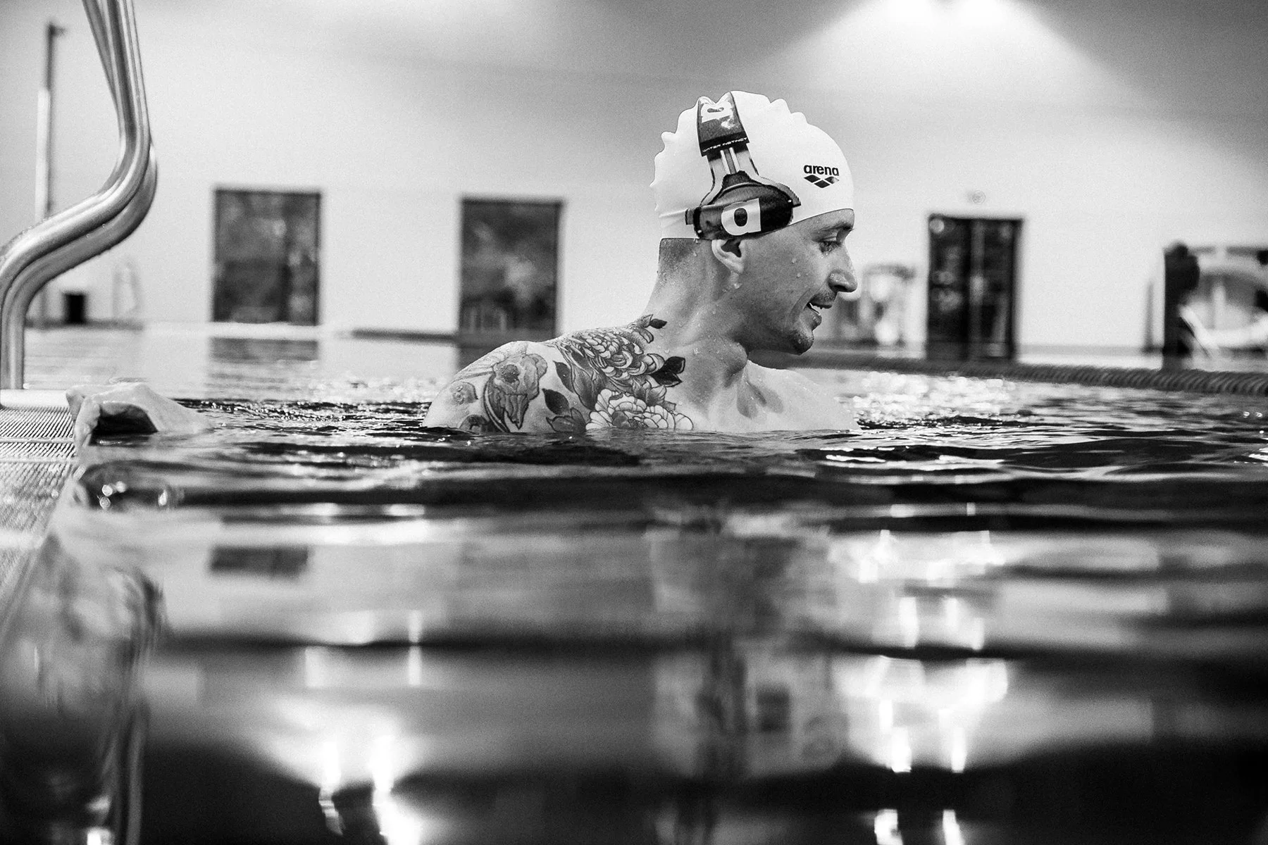 Portrait documentaire en noir et blanc d'un nageur tatoué au bord d'un bassin.