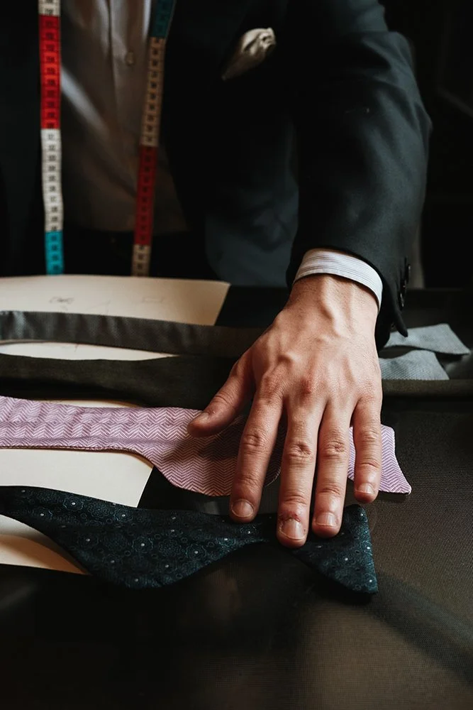 Une main d'homme en costume ajustant des cravates ou tissus de costume de différentes couleurs et textures, sur une table.
