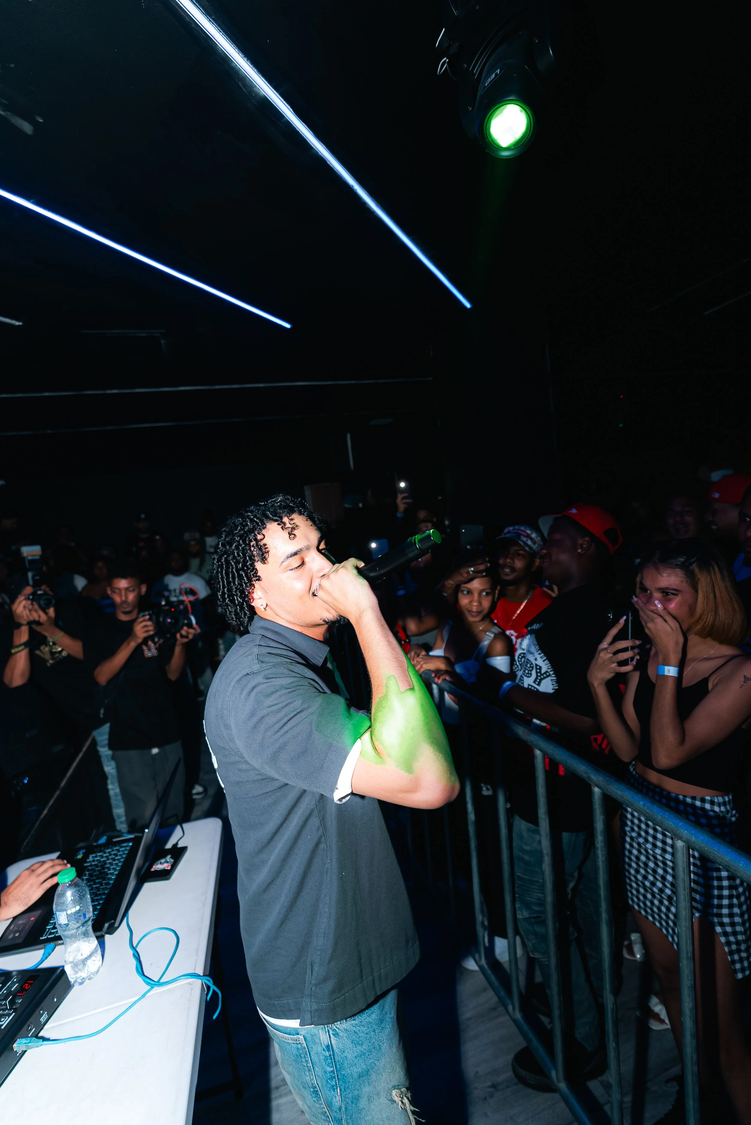 Performer singing on stage at a concert with audience and photographers capturing the moment.